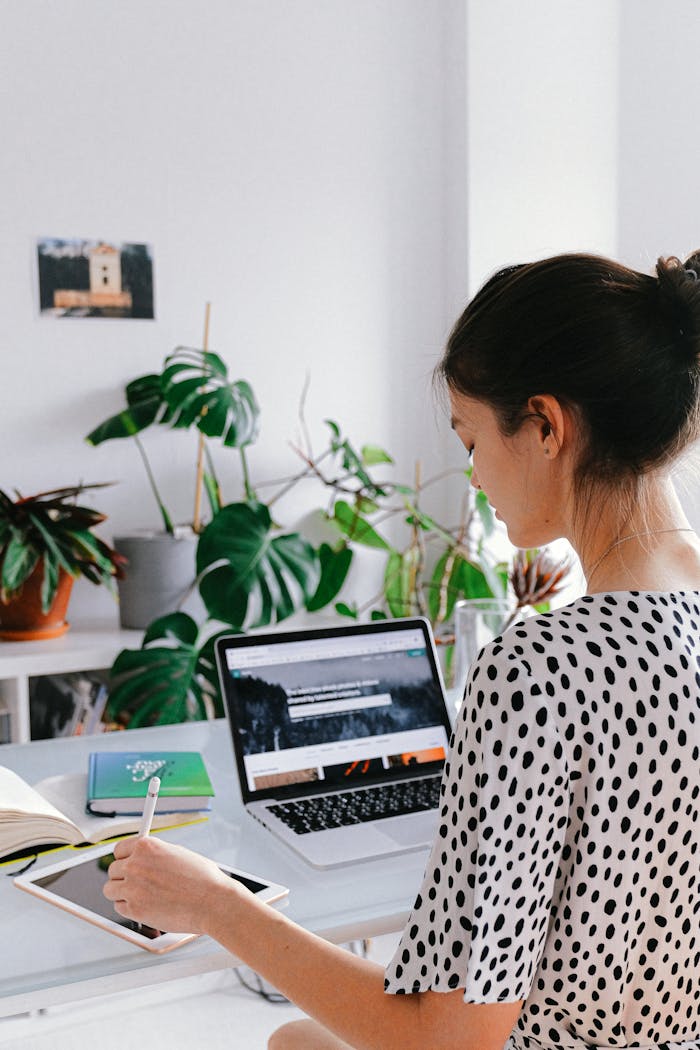 Woman working in a stylish home office with laptop and tablet, embracing remote work lifestyle.
